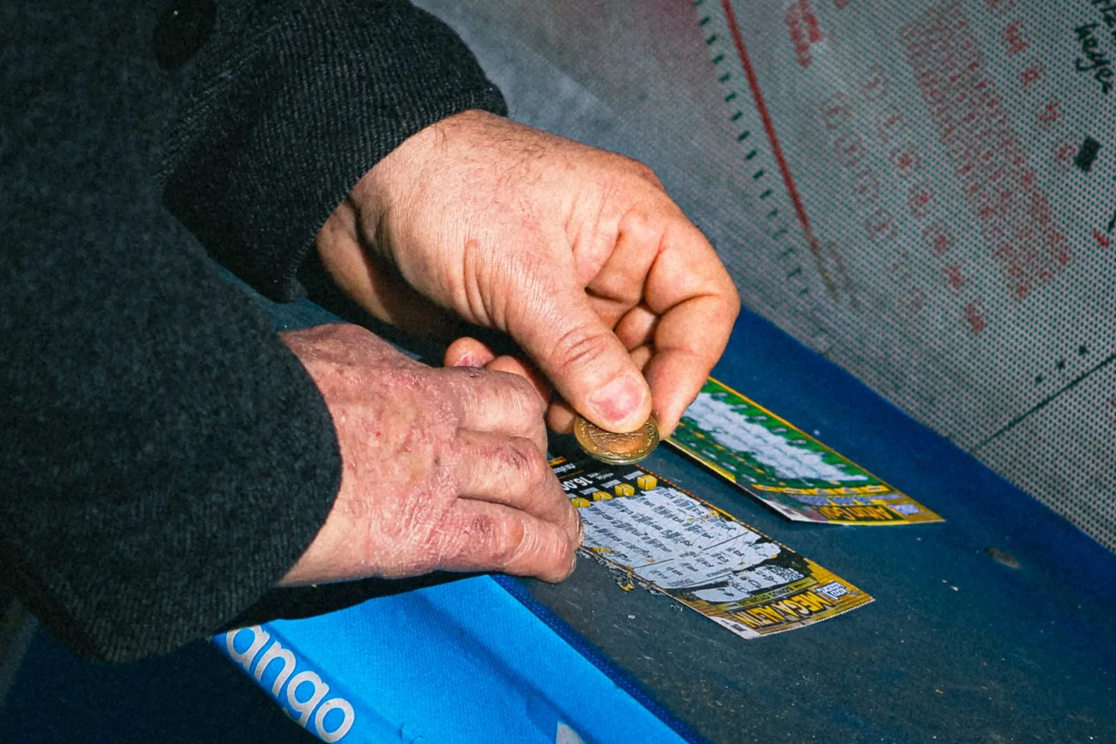 Close-up of hands using a coin to scratch a lottery ticket on a blue table